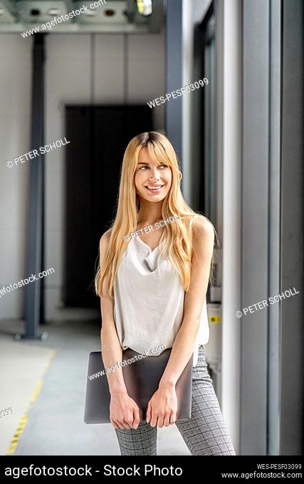 Young blond businesswoman holding laptop at workplace