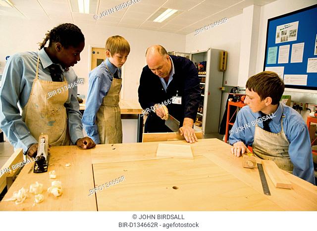Woodwork teacher showing students how to saw wood in Design technology lesson