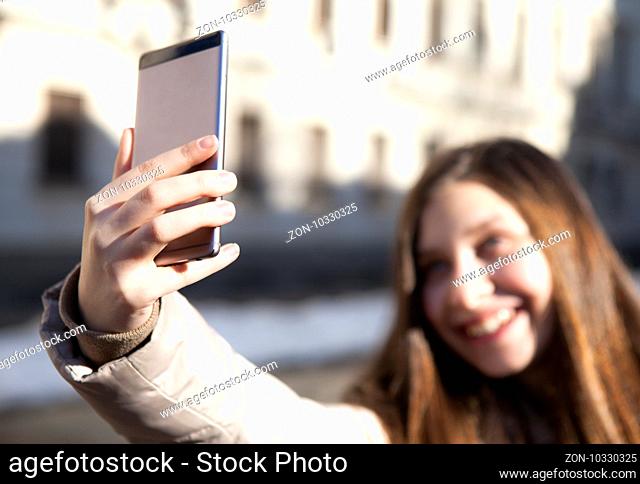 Gorgeous beautiful brunette young woman taking a selfie with smart-phone at the city street background