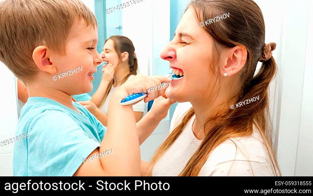 Funny toddler boy cleaning and brushing mothers teeth. Concept of family hygiene and teeth healthcare