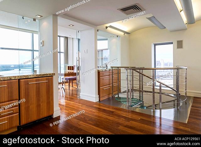 Steel and tempered glass spiraling staircase in home office with exotic wood cabinets and floorboards inside a modern luxurious multistory penthouse condominium...