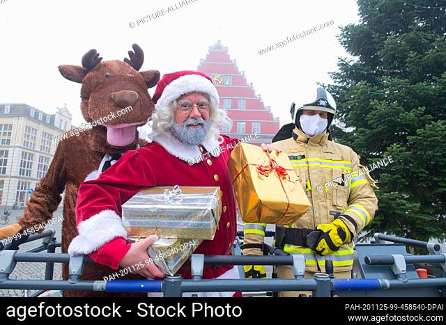 25 November 2020, Mecklenburg-Western Pomerania, Greifswald: An employee of the city of Greifswald dressed as Santa Claus stands in a crane truck on the...