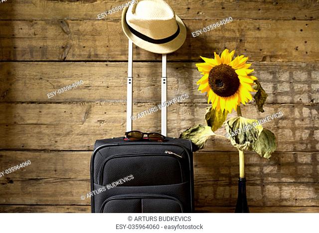 Travel concept. Suitcase, hipster hat, sunflower and sunglasses on wooden wall background