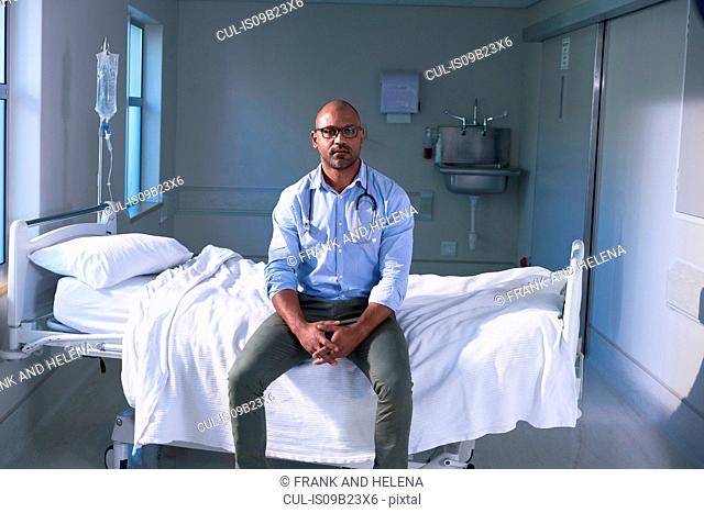 Portrait of mature male doctor sitting on hospital bed in ward