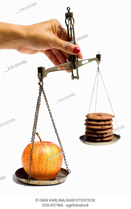 A woman's hand holding a scale weighing apples and cookies