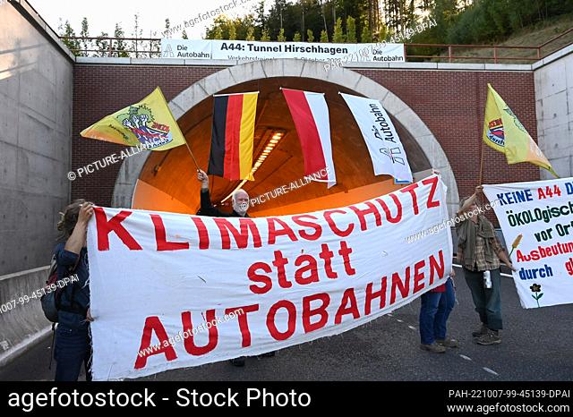 07 October 2022, Hesse, Helsa: Environmental activists stand with banners in front of the Hirschhagen tunnel portal during the opening of the A 44 highway...