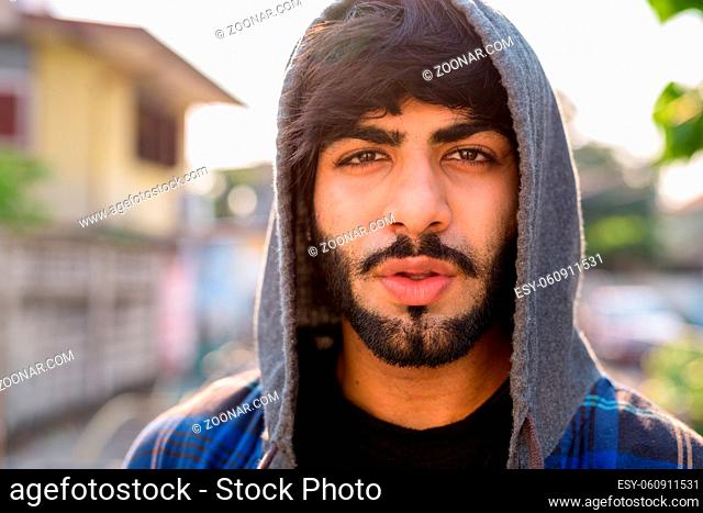 Portrait of young handsome bearded Indian hipster man in the streets outdoors