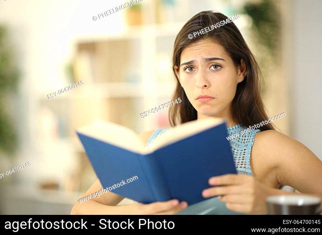 Sad book reader looking at camera sitting at home