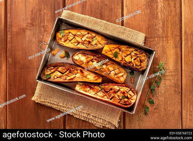 Baked eggplants with garlic and oregano, shot from above on a dark rustic wooden background with a place for text