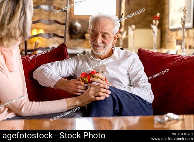 Senior man holding gift sitting by woman on sofa at boutique hotel