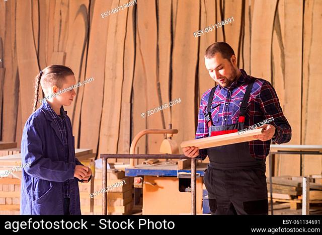 Young teen boy in blue robe, apprentice at carpentry shop learning how to work with wood. Young boy at first job while studying to be a carpenter