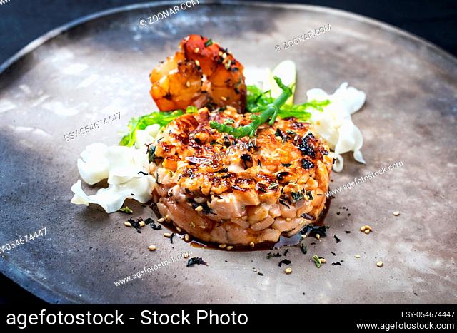 Gourmet salmon fish tartar raw from salmon fillet with glasswort, Japanese noodles and spice as closeup on a modern design plate