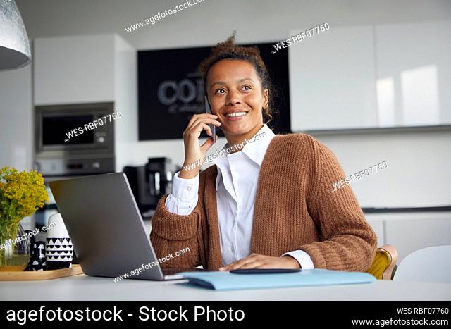 Portrait of smiling businesswoman on the phone in kitchen looking at distance