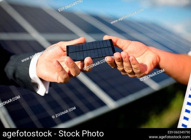 Close up view of photovoltaic item, solar panel in backstage. Hands of two men holding photovoltaic detail
