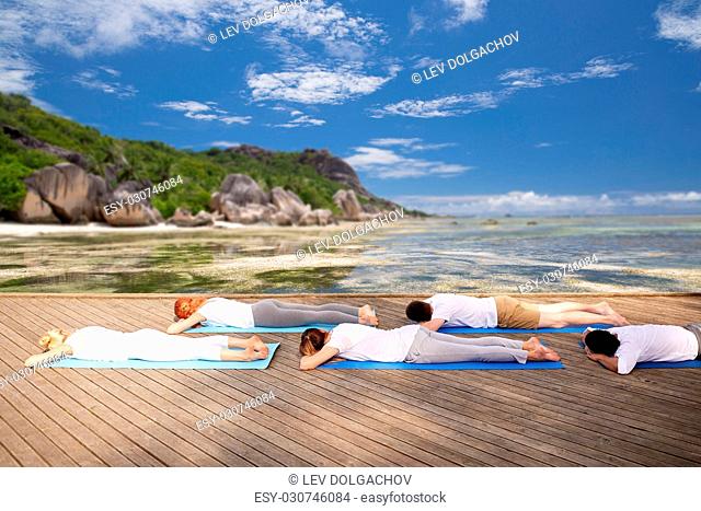 fitness, yoga and sport concept - group of people lying on mats over exotic tropical beach
