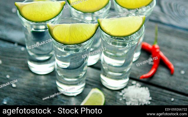 From above tequila shots served with lime and salt on wooden table with pepper
