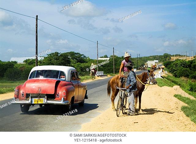 Classic American car passing by a cowboy and a cyclist talking on a countryside road, Cuba
