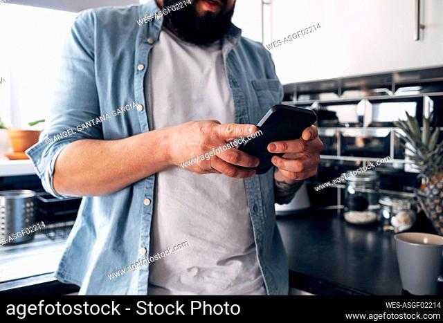 Man using smart phone in kitchen at home