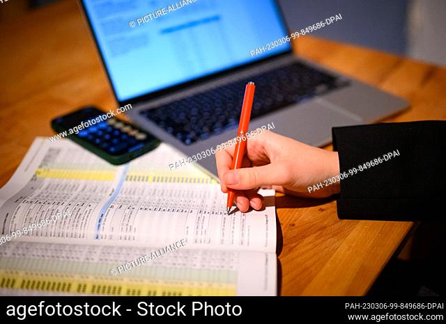 PRODUCTION - 12 February 2023, Hamburg: A woman sits at her laptop with financial spreadsheets and calculator app on her phone (posed scene)