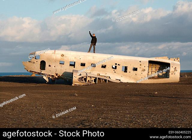 Old crashed plane in Iceland with traveler posing on the top