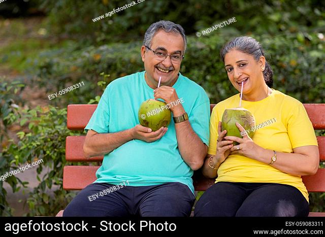 A HAPPY COUPLE LOOKING AT CAMERA WHILE DRINKING COCONUT WATER