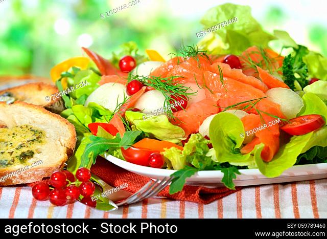 Gemischter Sommersalat mit Melonenkugeln, Johannisbeeren und Räucherlachs, mit getoastetem Ciabattabrot mit Kräuterbutter serviert - Summer salad with honeydew...