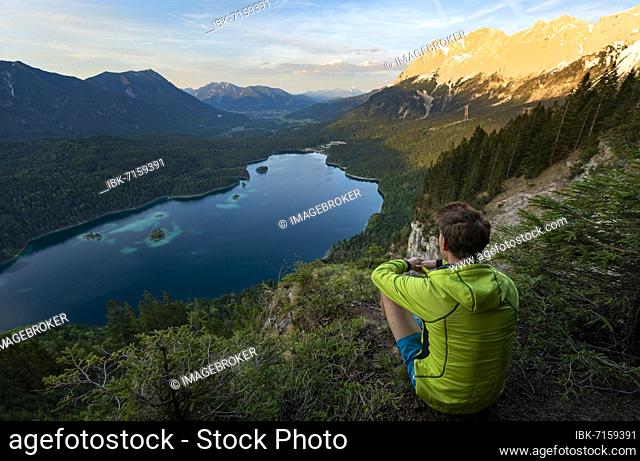 Young man looking over the Eibsee lake at sunset, Zugspitze and Zugspitzmassiv, alpenglow, behind Bishop and Krottenkopf, Wetterstein Mountains, near Grainau