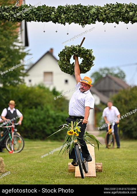 12 August 2023, Brandenburg, Heinersbrück: A participant in the traditional Sorbian-Wendish wreath piercing, tries to get a wreath off a holder with a stick...