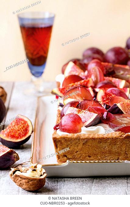 Homemade rectangular Tart with red Grapes, Figs, walnuts and Whipped cream in white ceramic plate over white wooden table