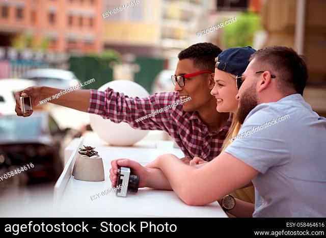 Picture of happy friends making selfies on mobile or smart phone outdoors. People spending free time in city centre. People posing for camera