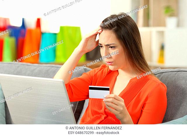 Worried shopper buying online with credit card sitting on a couch in the living room at home