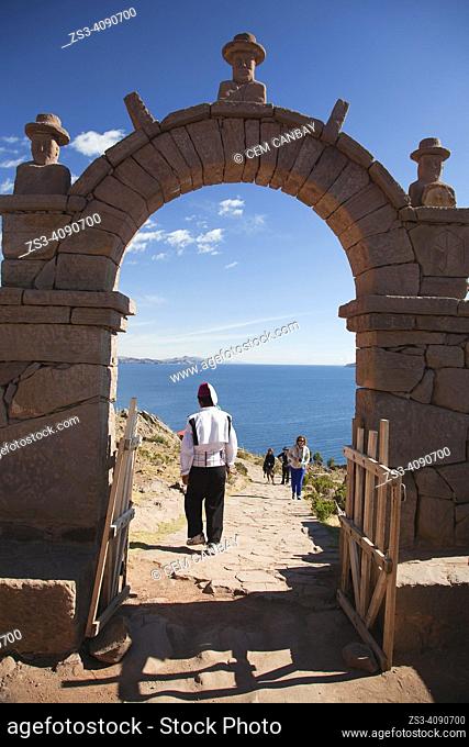 Indigenous man in traditional dress passing through a stone arch and walking down the beach, Taquile Island, Titicaca Lake, Puno Region, Peru, South America