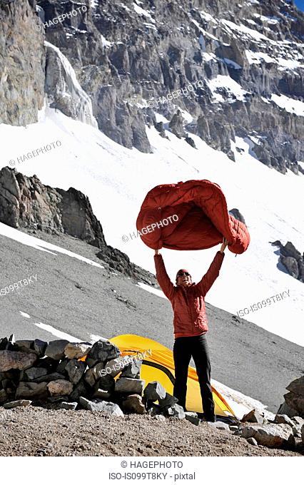 Woman shakes her sleeping bag at Camp One on Aconcagua in the Andes Mountains, Mendoza Province, Argentina