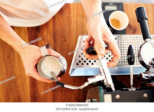 Overhead shot of a barista's hands using an espresso machine to steam some fresh milk in a stainless steel jug