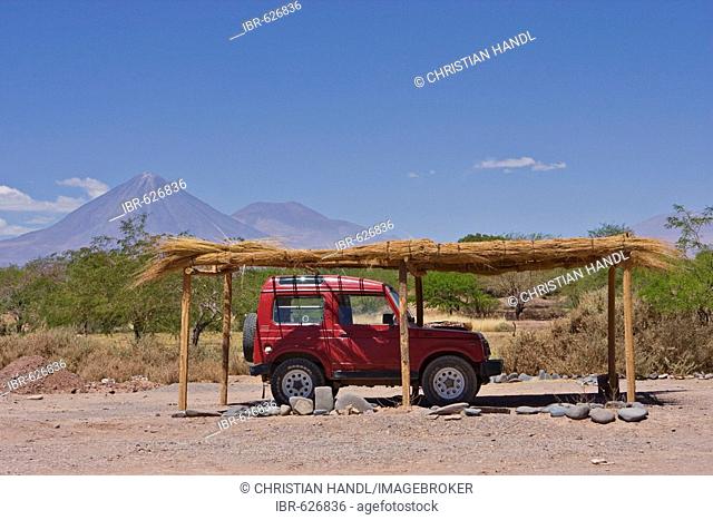 Four-wheel drive vehicle parked under sun shade in front of a small clay house, Licancabur Volcano in background, San Pedro de Atacama, Chile, South America