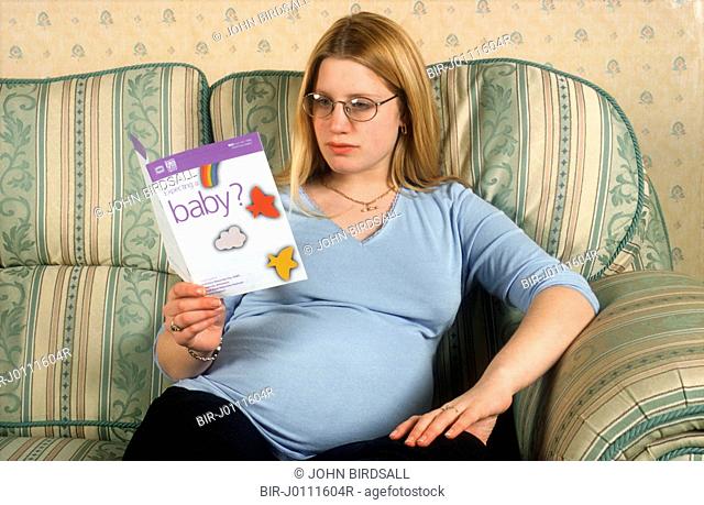 Pregnant teenage girl reading information leaflet about pregnancy