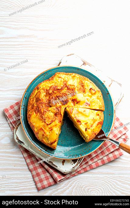 Homemade Spanish tortilla with one slice cut - omelette with potatoes on plate on white wooden rustic background top view