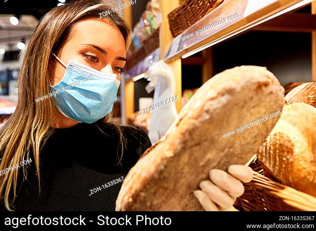 Kundin mit Mundschutz beim Brot kaufen im Supermarkt bei Covid-19 Pandemie