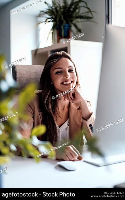 Cheerful businesswoman sitting with hand on chin at home office