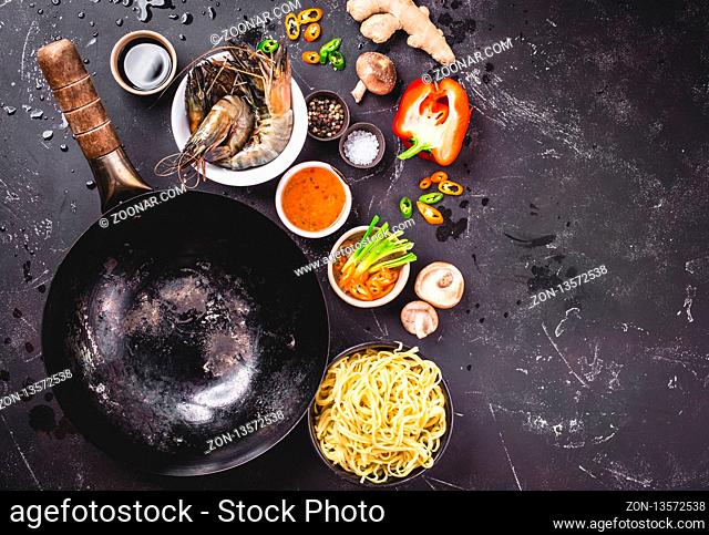 Asian food cooking concept, dark background. Empty wok pan, noodles, vegetables stir fry, shrimps, chopsticks. Space for text. Asian/Chinese food