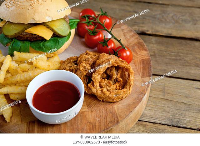 Hamburger, onion ring, tomato sauce, cherry tomato and french fries on chopping board