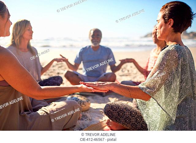 Serene people meditating in circle on sunny beach during yoga retreat
