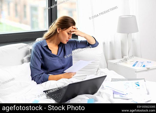 young woman with laptop and papers in bed at home