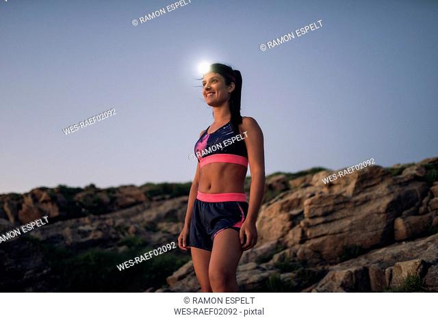Sportive woman with headlamp standing on rocky coast