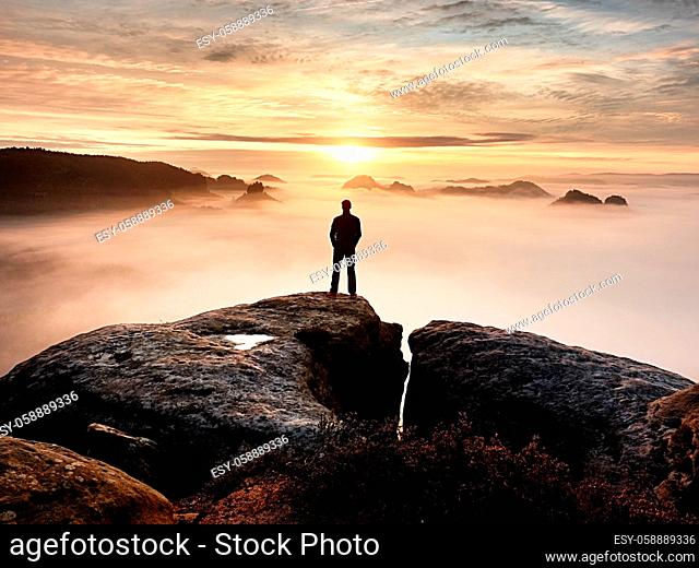Man silhouette stay on sharp rock peak. Satisfy hiker enjoy view. Tall man on rocky cliff watching down to landscape. Vivid and strong effect