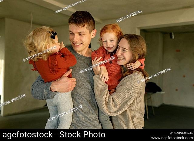 Smiling father and mother carrying daughters at home