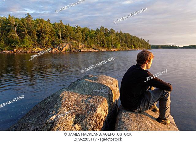 A man sitting on a rock as the sun sets over Georgian Bay. Massasauga Provincial Park, Ontario, Canada