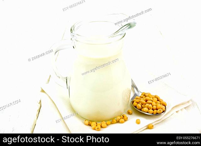 Soy milk in a jug, soybeans in a spoon on a napkin against the background of a light wooden board