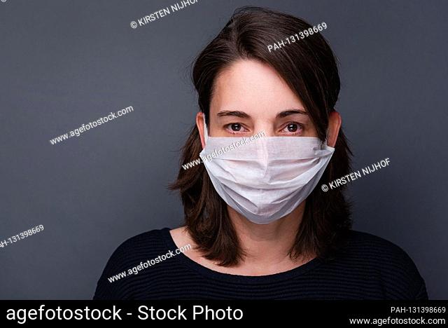 Symbolic photo on the subject of the corona pandemic, Covid-19 - A woman wears a hygiene mask and stands against a gray background, taken on March 31