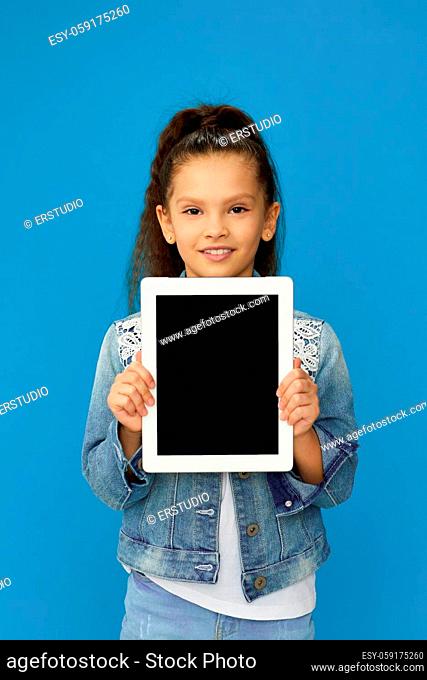 smiling little child girl shows empty tablet on blue background